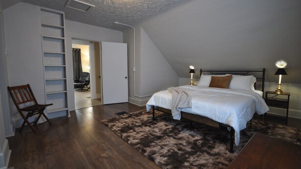 A bedroom with a bed, a chair, a desk, a wardrobe, and a ceiling light. - Comfy Rustic Retreat 2 blocks from Mayo Hospital and Bethany College. (Mankato)