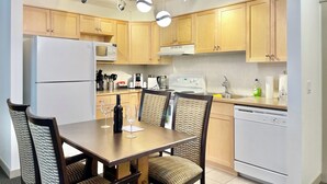 Une cuisine moderne avec des meubles en bois, un réfrigérateur blanc, un four à micro-ondes, une cuisinière et un évier. On y trouve une table à manger avec des chaises et un lustre au-dessus.