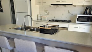 A modern kitchen with a central island, bar stools, a stainless steel sink, a microwave, and a stove. - Farm cottage in 2.3 acres. Fully renovated for your comfort.  (Newmerella)