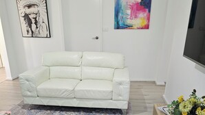 A modern living room with a white leather sofa, a patterned rug, a round white coffee table, and a wooden side table with a vase of flowers. - Farm cottage in 2.3 acres. Fully renovated for your comfort.  (Newmerella)