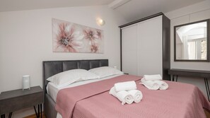 A bedroom with a bed, pillows, a bedside table, a wall-mounted mirror, and a painting.