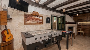 Una habitación acogedora con una mesa de fútbol, una guitarra y una pared de piedra.