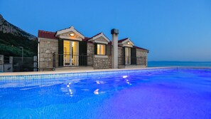 Un edificio de piedra con piscina, destacando su fachada de piedra, techos de tejas rojas y vistas al mar.