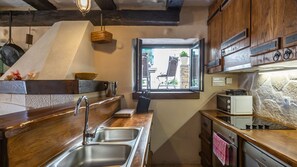 A compact kitchen with wooden countertops, a stainless steel sink, a window with a view, and a stone wall.