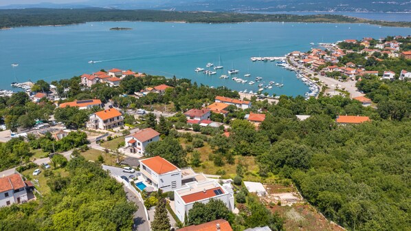 An aerial view of a coastal village with houses, a marina, and boats.