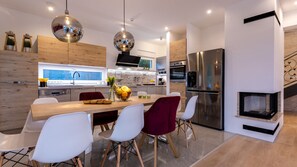 A modern kitchen with a wooden dining table, white chairs, and a fruit bowl.