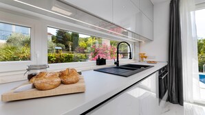 A modern kitchen with a large window, a black faucet, and a wooden cutting board with bread.