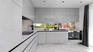 A modern kitchen with white cabinetry, a black sink, and a window with a view of greenery.