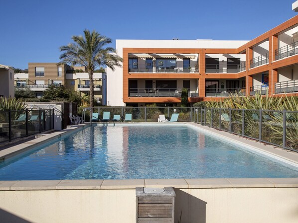 A swimming pool with lounge chairs and a modern building with balconies in the background. - Le Garden Beach by Interhome (Villeneuve-Loubet)