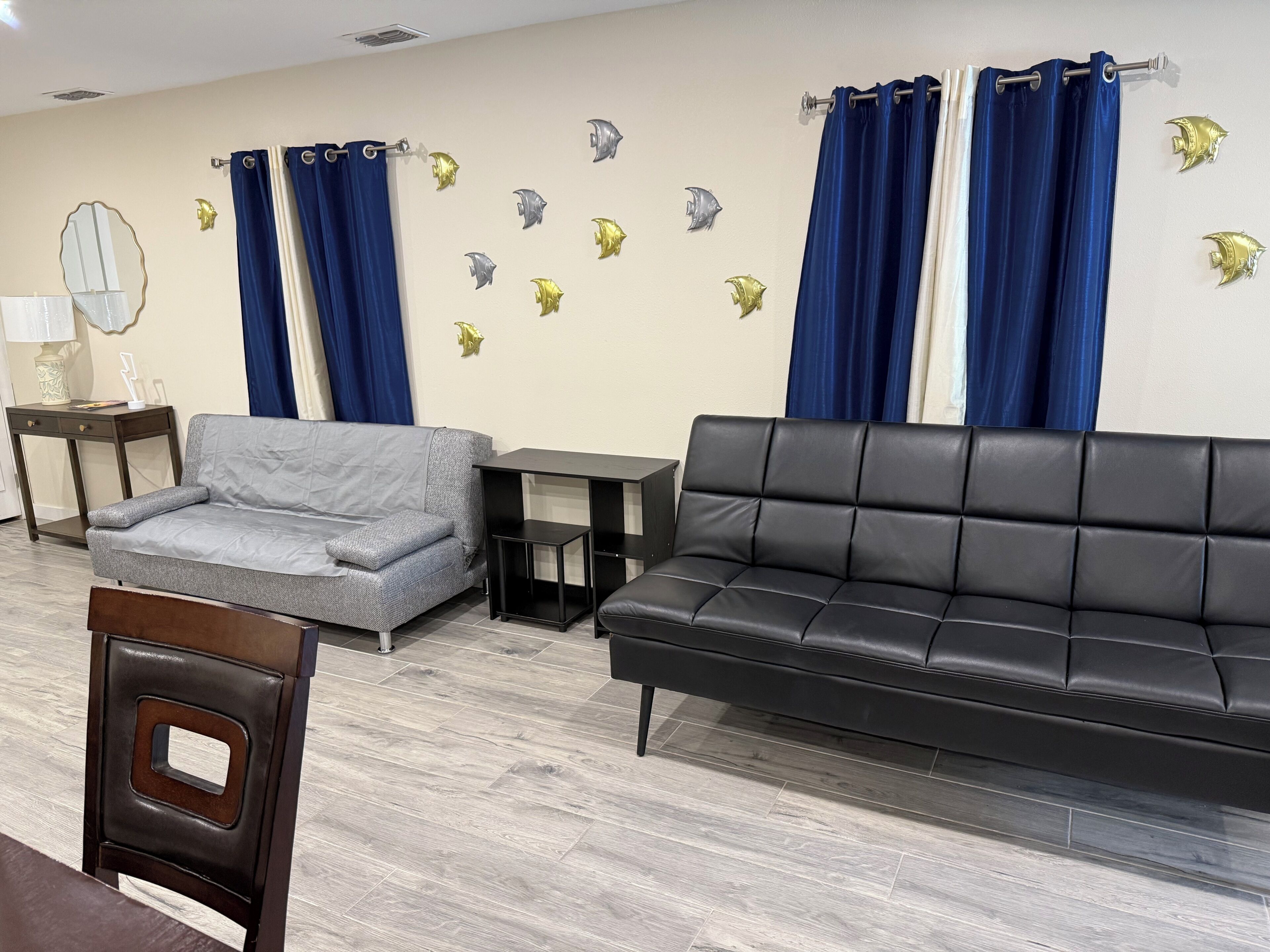 Ein Wohnzimmer mit grauem Sofa, einem schwarzen Ledersofa, einem kleinen Tisch und dekorativen Wandaufklebern mit Fischmotiven.