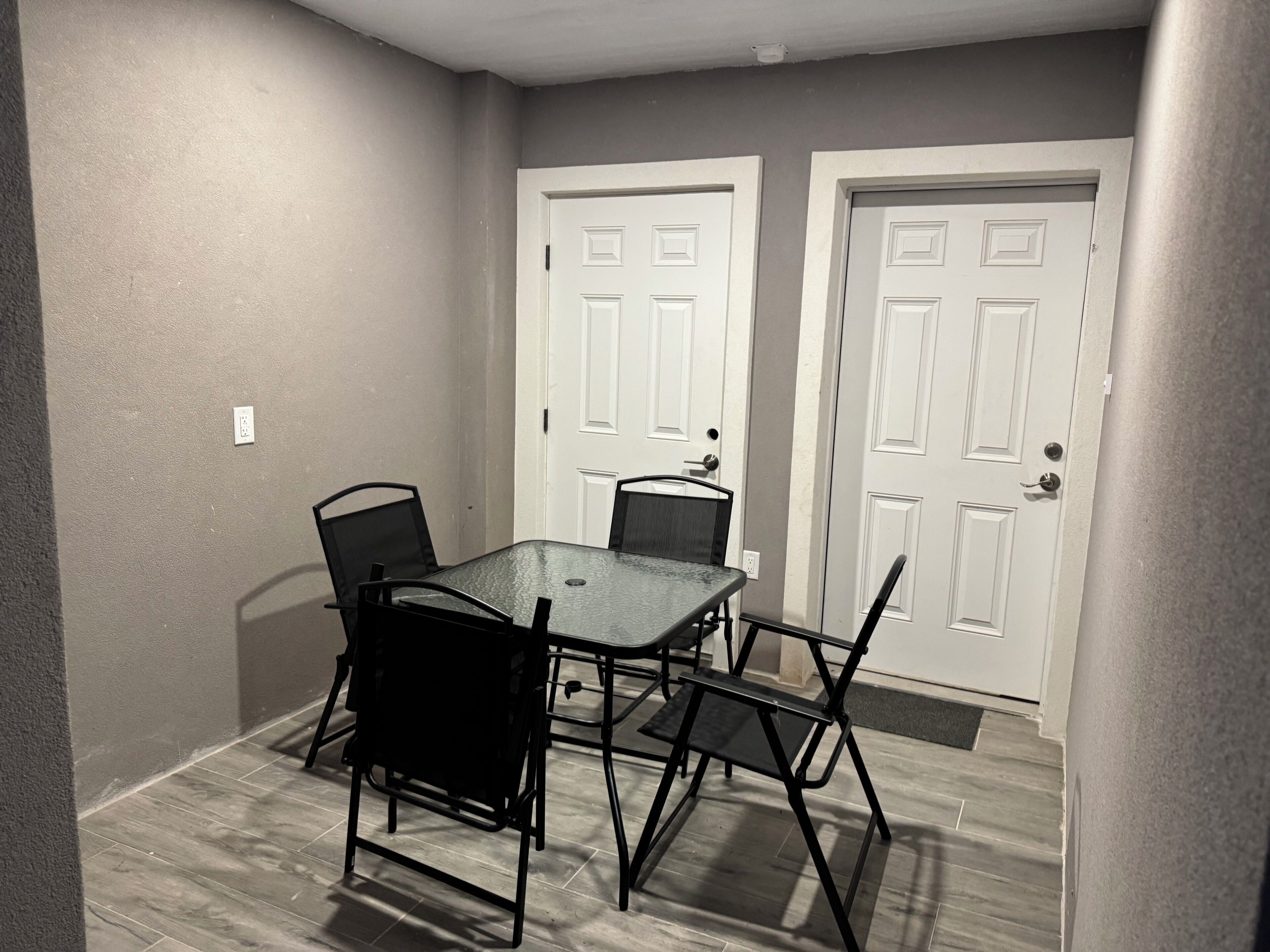 A small dining area with a table and four chairs, two white doors, and a light switch on the wall.