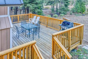 A wooden deck with a table and chairs, a grill, and a view of the surrounding forest. - Beautiful Homewood Retreat with Deck and Grill (Homewood)