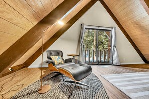 Un dormitorio estilo loft moderno con techo inclinado, sofá de cuero negro, suelo de madera y un gran ventanal con cortinas.