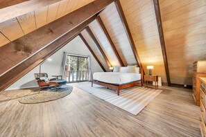 A bedroom with a sloped ceiling, a bed, a nightstand, a dresser, and a view of the outdoors. - Beautiful Homewood Retreat with Deck and Grill (Homewood)
