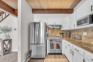 Una cocina moderna con electrodomésticos de acero inoxidable, armarios blancos y techo de madera.