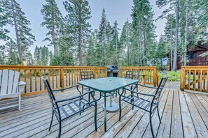 A wooden deck with a table and chairs, surrounded by tall trees. - Beautiful Homewood Retreat with Deck and Grill (Homewood)