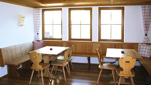 A room with wooden walls and floors, featuring a wooden table and bench seating, large windows with curtains, and a radiator on the wall. - Holiday Home, Fiss (Fiss)
