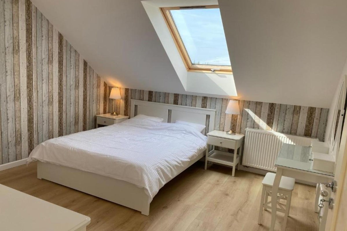 Une chambre avec un plafond en pente, un puits de lumière, un lit, des tables de chevet, un miroir et un radiateur.