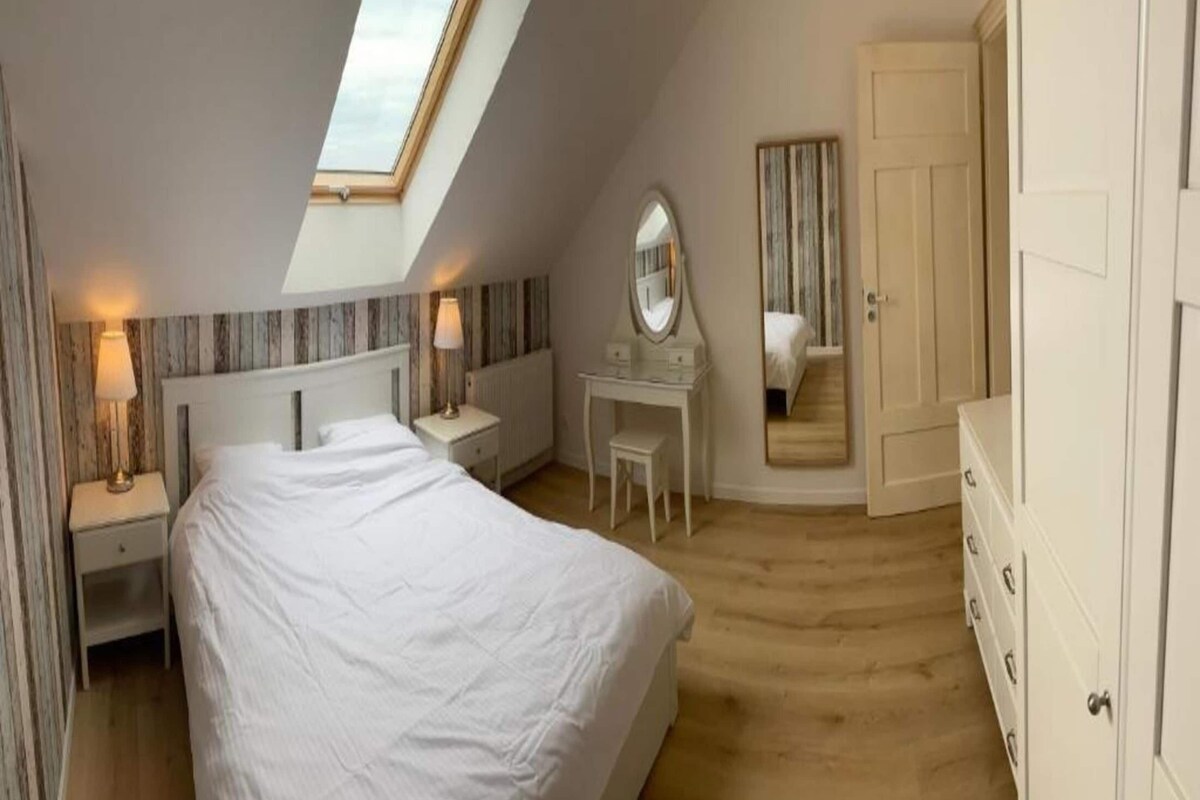 Ein Schlafzimmer mit Dachfenster, einem Bett, einem Schreibtisch mit Spiegel und einem Kleiderschrank.