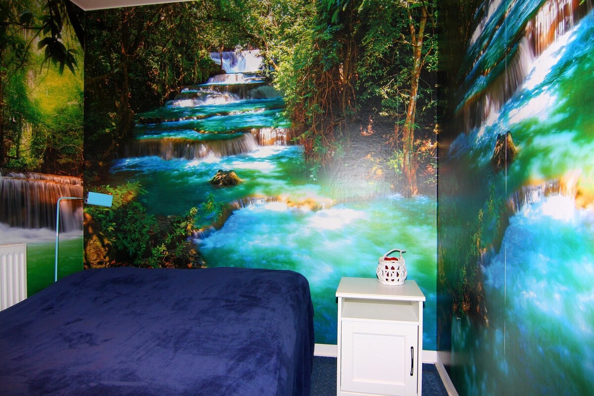 A bedroom with a large mural of a waterfall, a bed, and a nightstand with a decorative item.