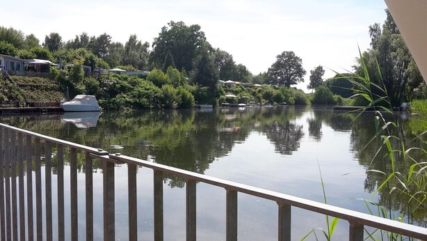 A calm river with a boat docked on the left, surrounded by lush greenery and trees.