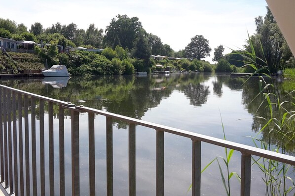 A calm river with boats, greenery, and a house in the background.