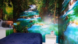 A bedroom with a large mural of a waterfall, a bed, and a nightstand with a decorative item.