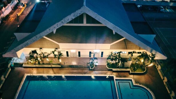 Una gran piscina con un diseño arquitectónico singular, rodeada de senderos bien iluminados y palmeras.