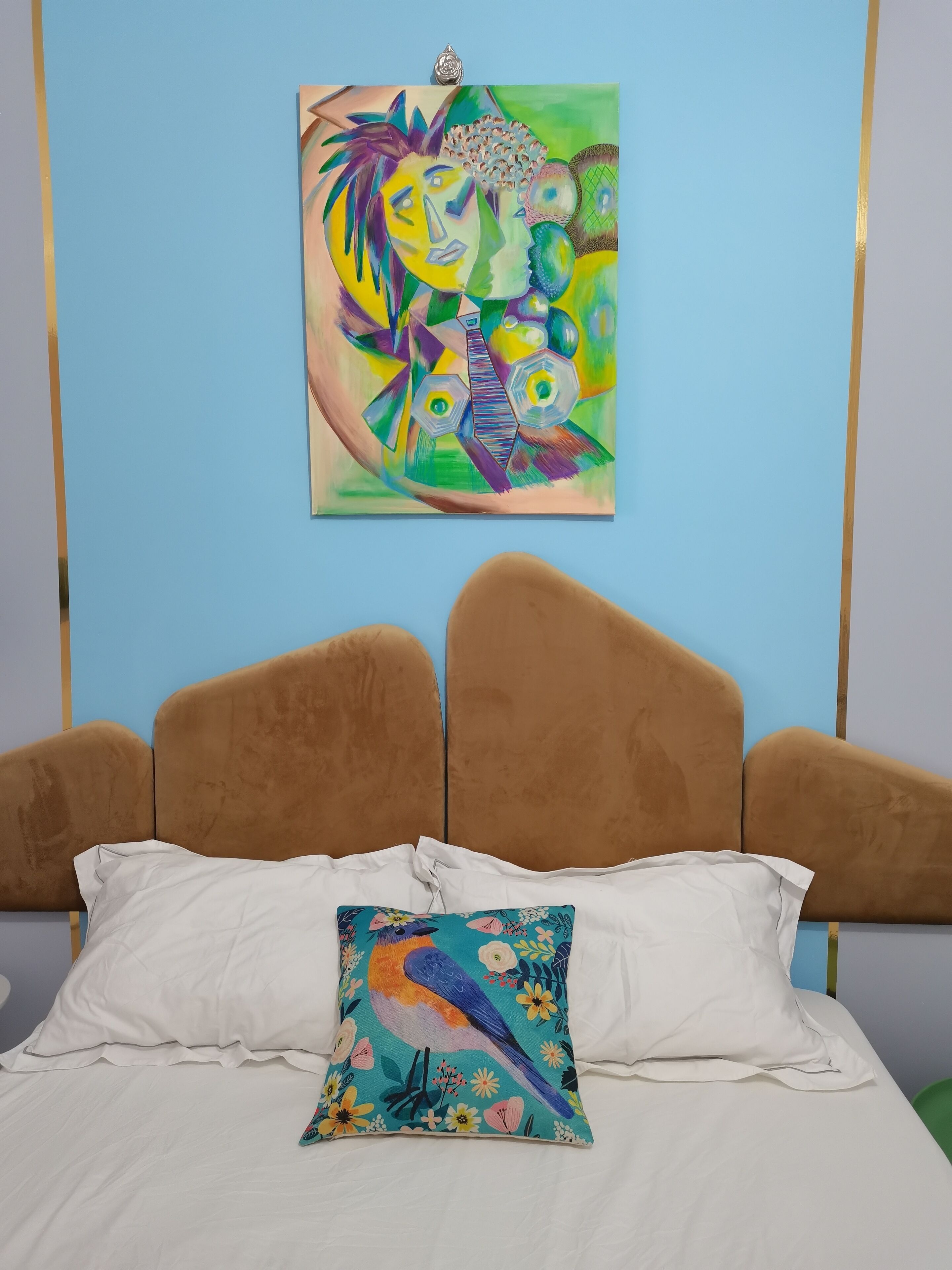 A bedroom with a bed, white pillows, and a colorful bird pillow.