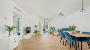 Un soggiorno moderno con pavimento in legno, un'area pranzo con sedie blu, una TV e una pianta.