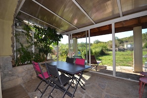 A covered patio with a table and chairs, stone walls, and a view of greenery. - Amazing Apartment in Lanas With Large Garden (Lanas)