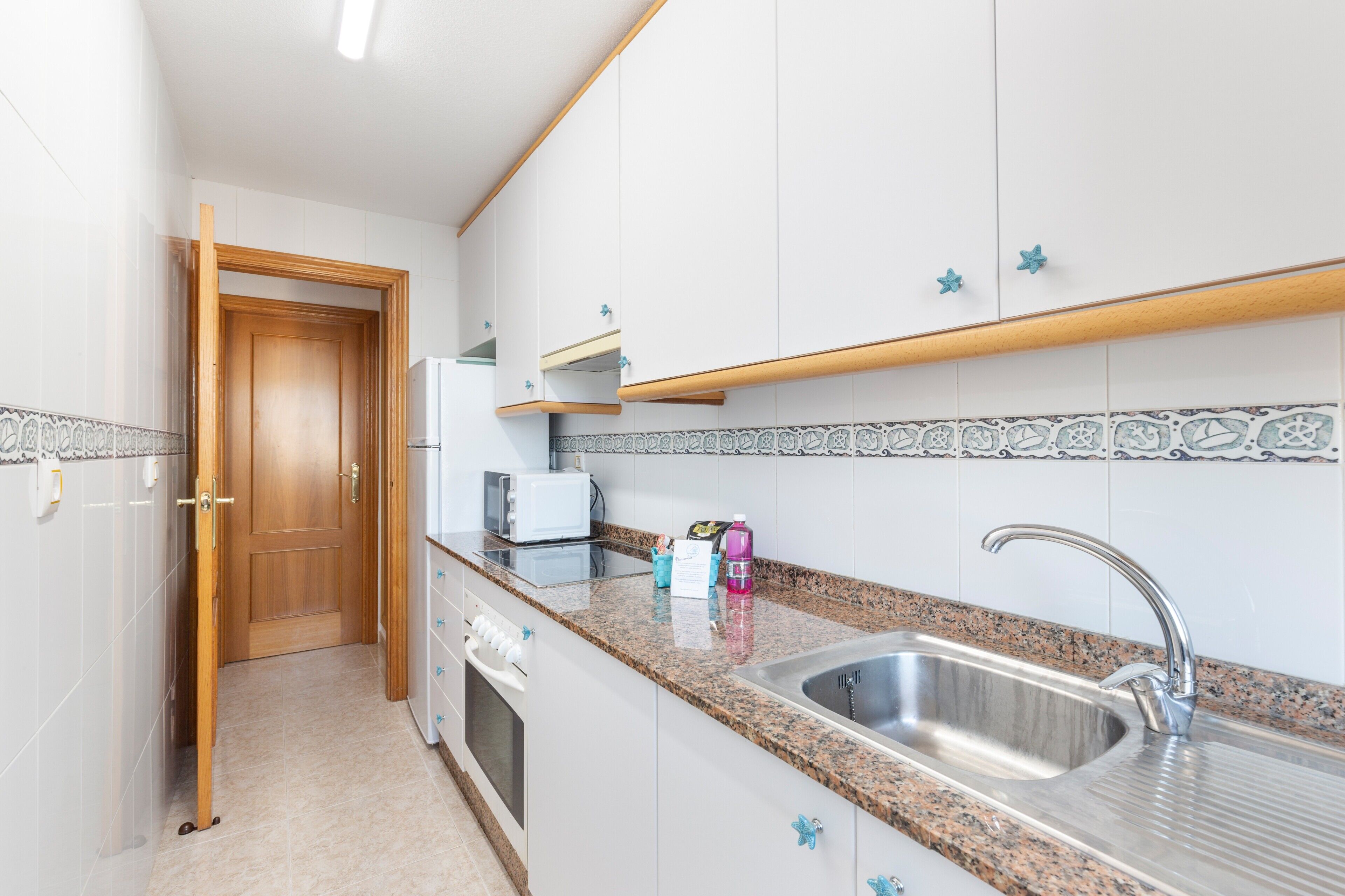 Une cuisine moderne avec des meubles blancs, un plan de travail en granit, un évier en acier inoxydable et une porte en bois.
