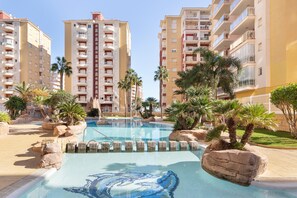 A swimming pool with a dolphin design, surrounded by palm trees and large rocks, with high-rise buildings in the background. - Apartment 'Mistral Apartment La Manga' with Sea View, Wi-Fi and Air Conditioning (San Javier)