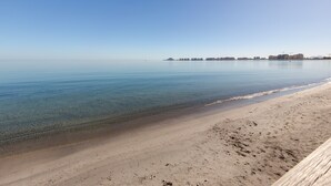 A beach with clear water, a sandy shore, and buildings in the distance. - Apartment 'Mistral Apartment La Manga' with Sea View, Wi-Fi and Air Conditioning (San Javier)