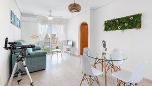 A modern living room with a telescope, a glass dining table, and a green sofa. - Apartment 'Mistral Apartment La Manga' with Sea View, Wi-Fi and Air Conditioning (San Javier)
