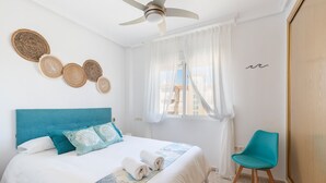 A bedroom with a bed, a ceiling fan, a window with curtains, a chair, and wall decor. - Apartment 'Mistral Apartment La Manga' with Sea View, Wi-Fi and Air Conditioning (San Javier)