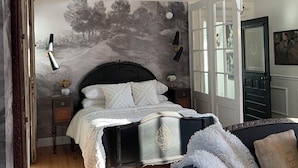 A bedroom with a bed, a nightstand, a dresser, a chandelier, and a door with glass panels. - The Chateau On Pascal (Rockport)