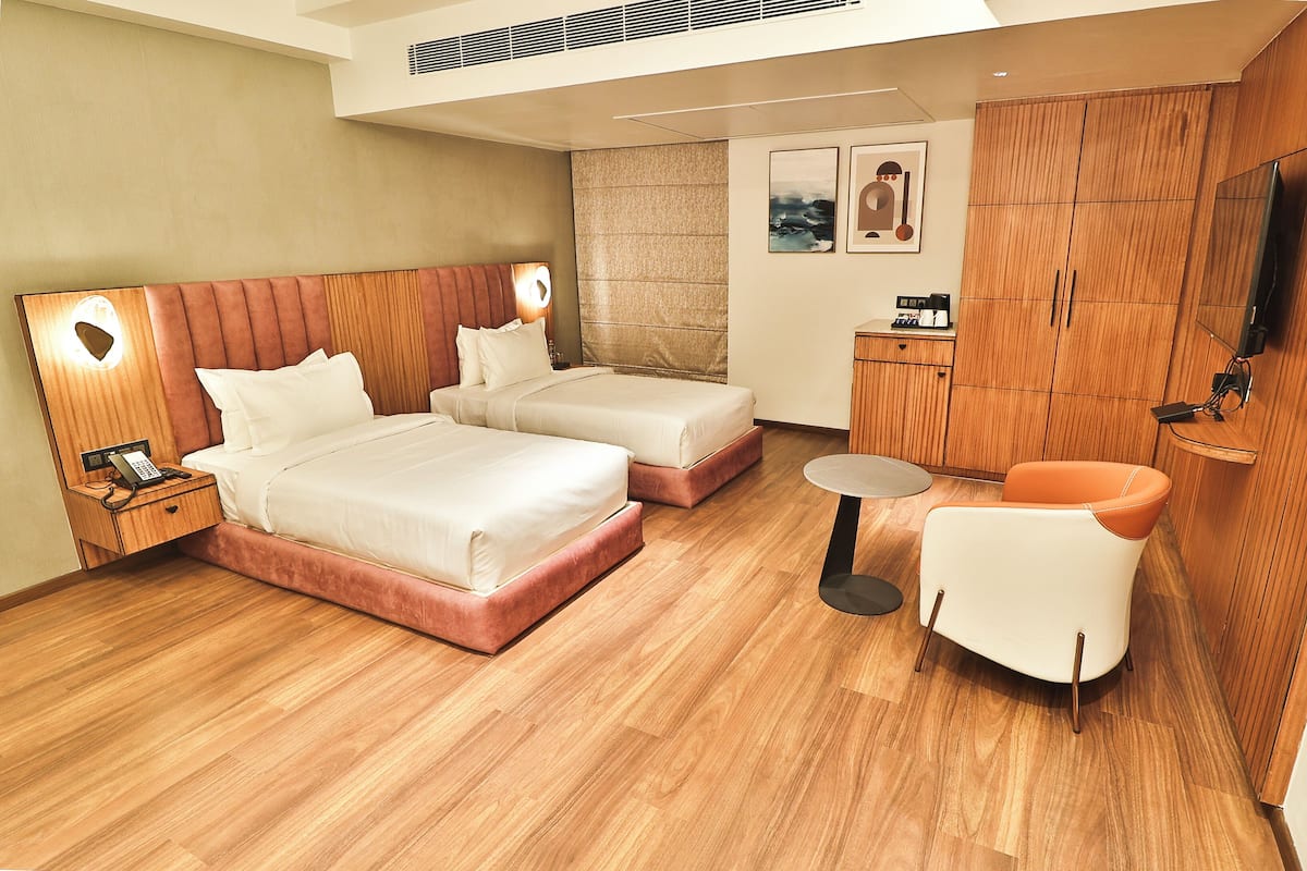 A hotel room with two beds, a small table, a chair, a TV, and a minibar.