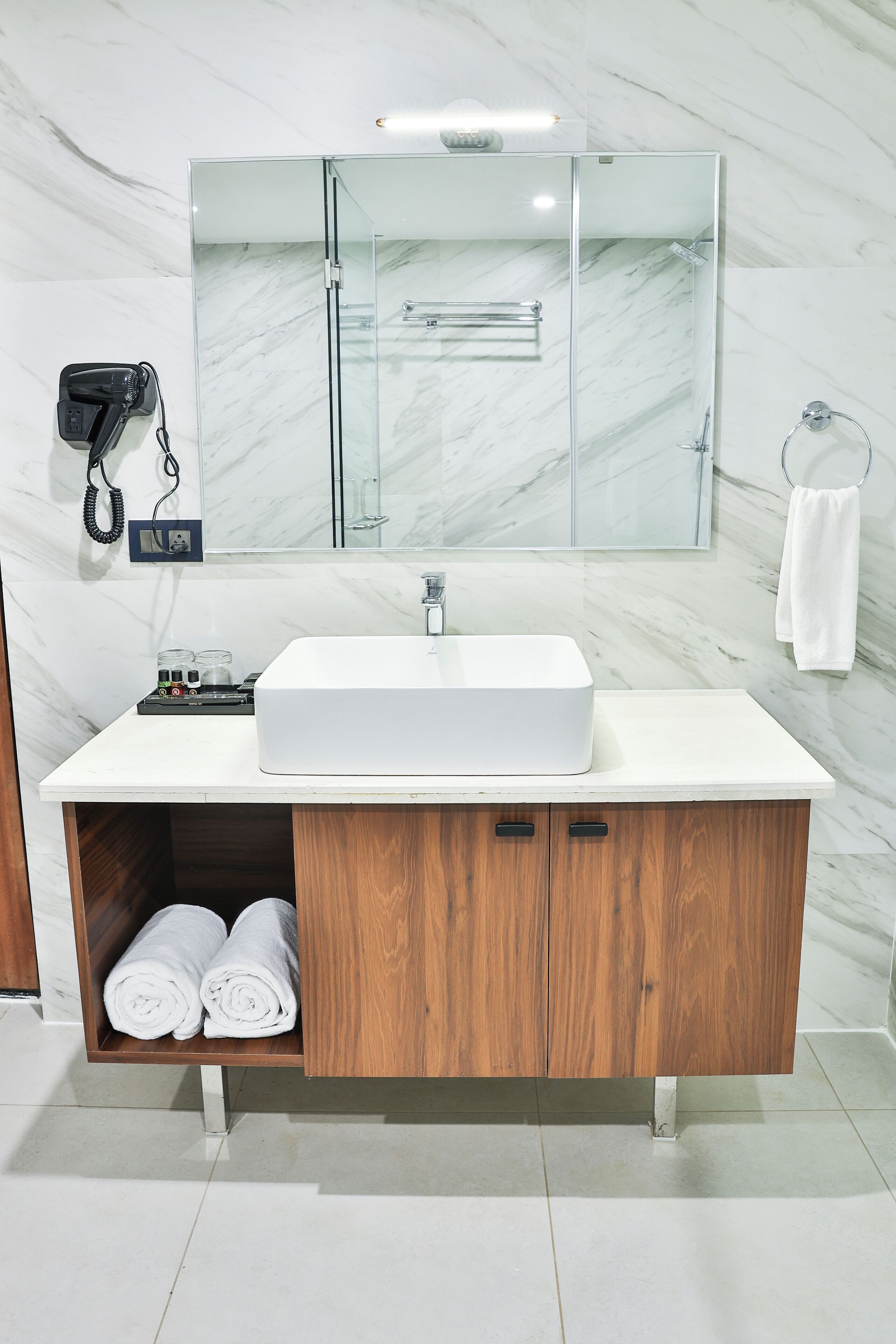 Une salle de bain avec un lavabo blanc, un meuble-lavabo en bois, des murs en marbre et une cabine de douche en verre.