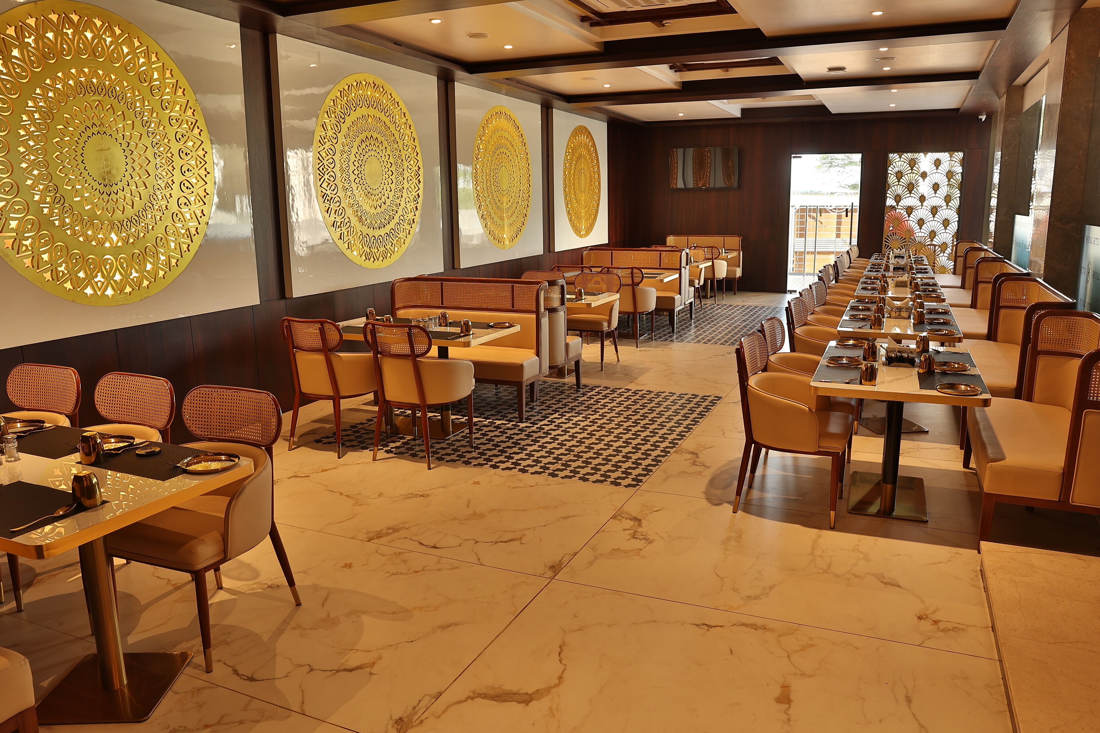 A spacious dining area with long tables and chairs, decorative wall panels, and a patterned floor rug.