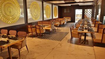 A spacious dining area with long tables and chairs, decorative wall panels, and a patterned floor rug.