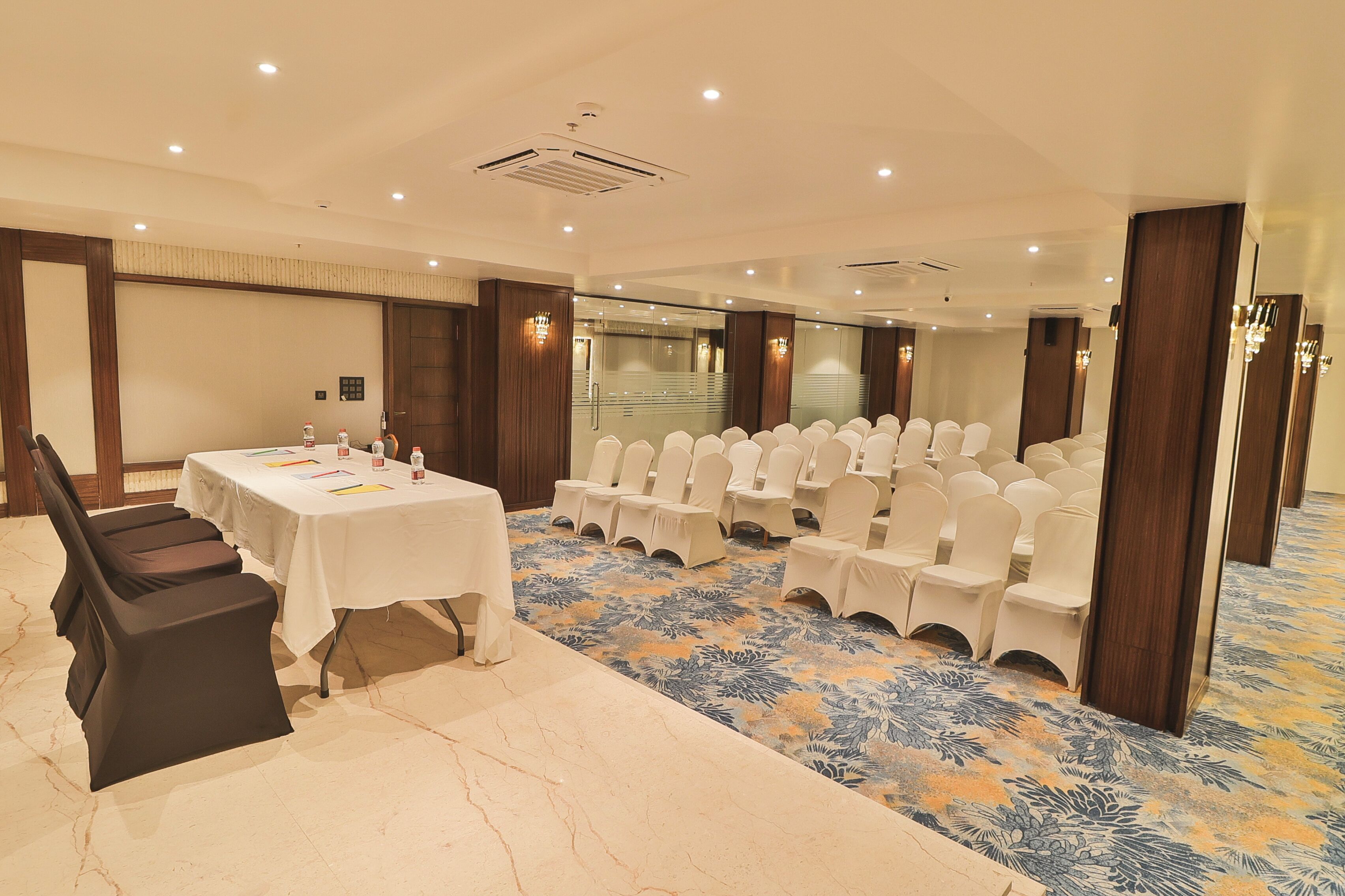 A conference room with a long table, rows of white chairs, and a patterned carpet.