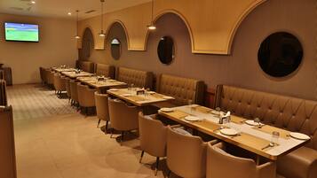 A restaurant with multiple tables and booths, a flat-screen TV on the wall, and a modern interior design.