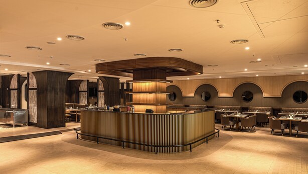 A modern restaurant with a central bar, multiple seating areas, and a polished tile floor. - Royal Ritis  (Belagavi)