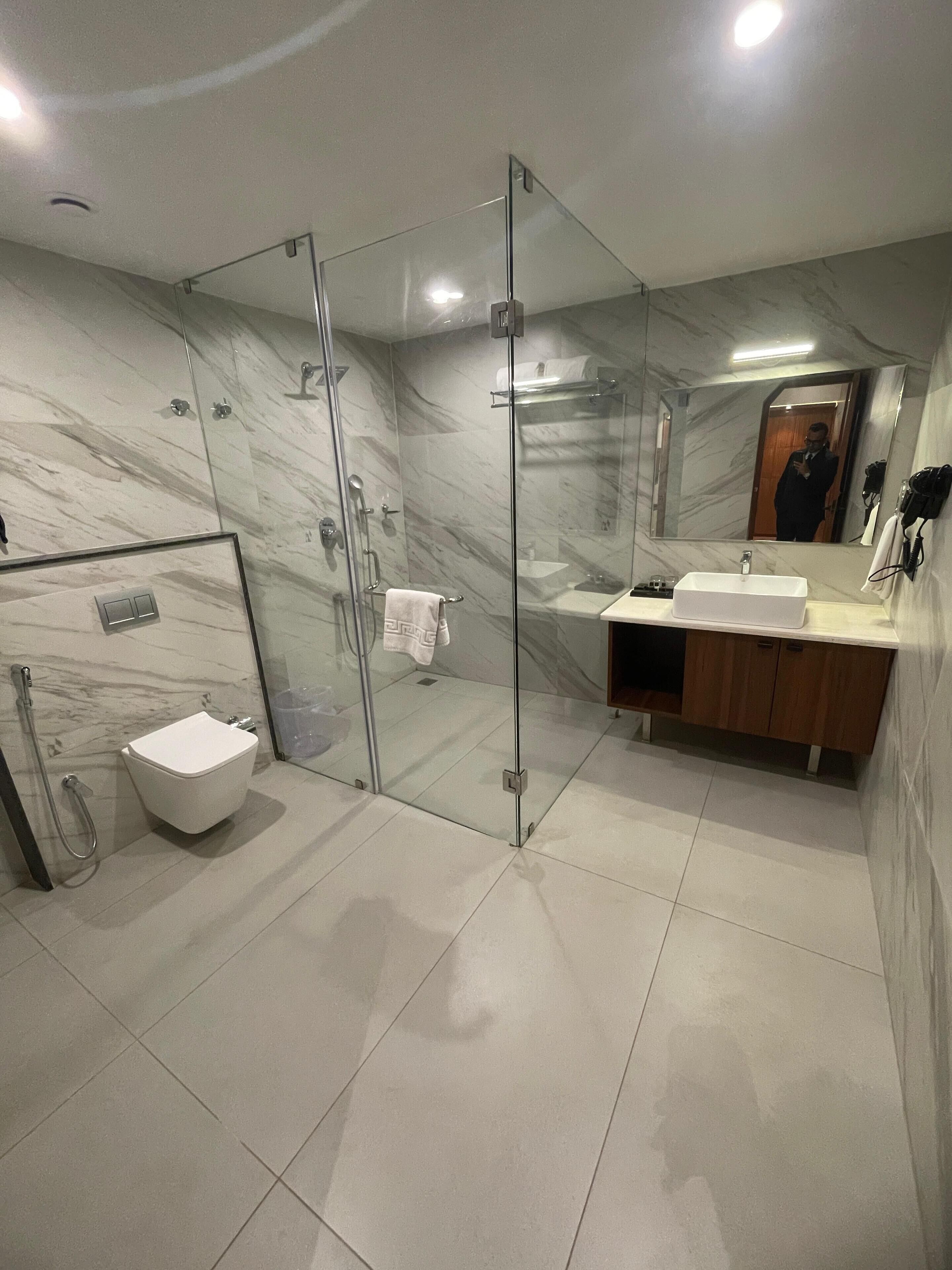 Een moderne badkamer met een douchecabine van glas, een witte wastafel en een vloer van marmer.