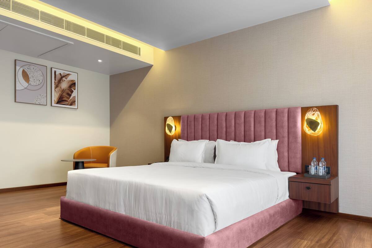 A modern hotel room with a large bed, a wooden floor, a small table, and a chair.