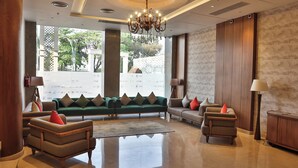 A spacious lobby with a green sofa set, two armchairs, a wooden cabinet, and a chandelier. - Royal Ritis  (Belagavi)