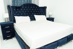 A bedroom with a tufted headboard, white bedding, and two bedside tables with lamps. - Apartament Luxury at Bonao (Bonao)
