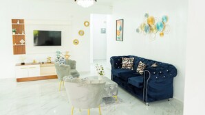 Ein modernes Wohnzimmer mit einem blauen Sofa, einem grauen Sessel, einem Marmortisch, einem Fernseher und einer Chandelier.