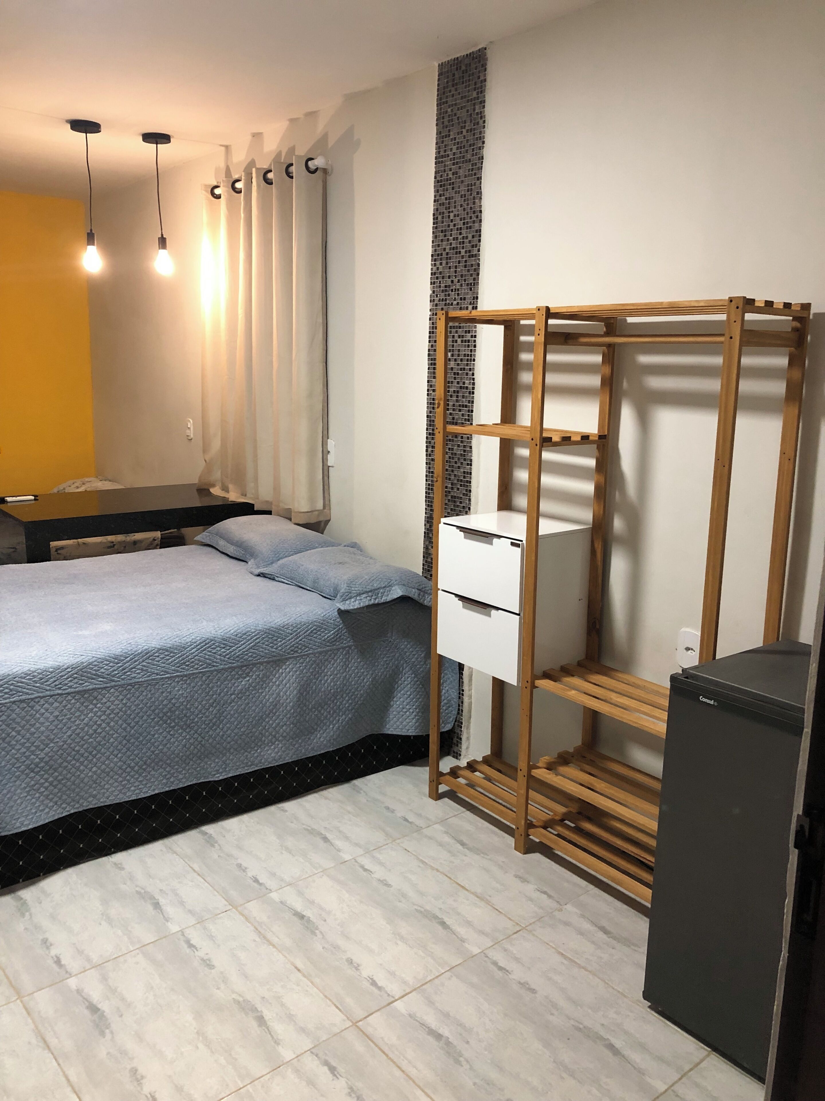 Un dormitorio con cama, armario, escritorio pequeño y refrigerador.
